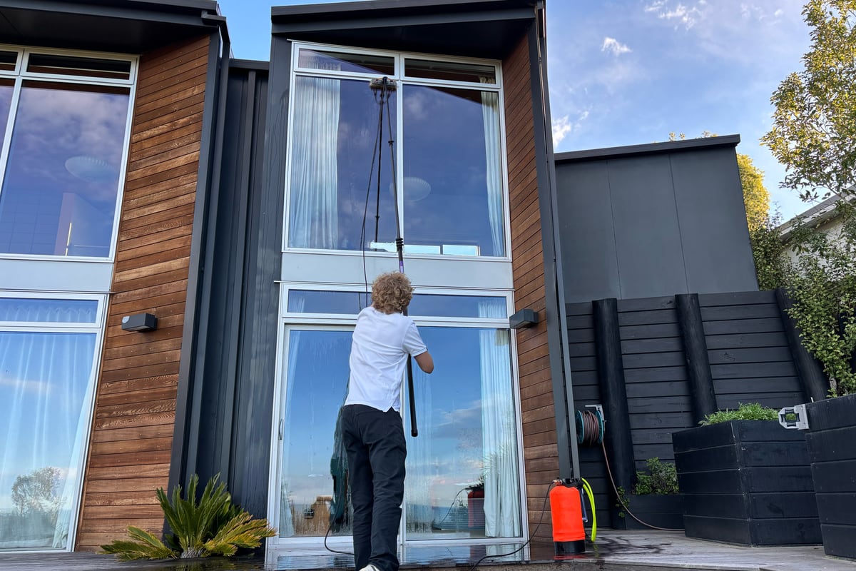 Luca cleaning a two-storey window from the ground with a water-fed pole
